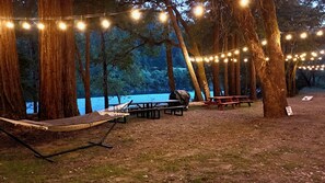 Eine Hängematte, Picknicktische und Lichterketten in einer bewaldeten Gegend mit einem See.