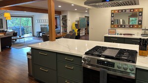 A modern kitchen with a central island, a gas stove, and a large range hood. - Large Cabin on Ave of Giants with private Eel River access (Miranda)