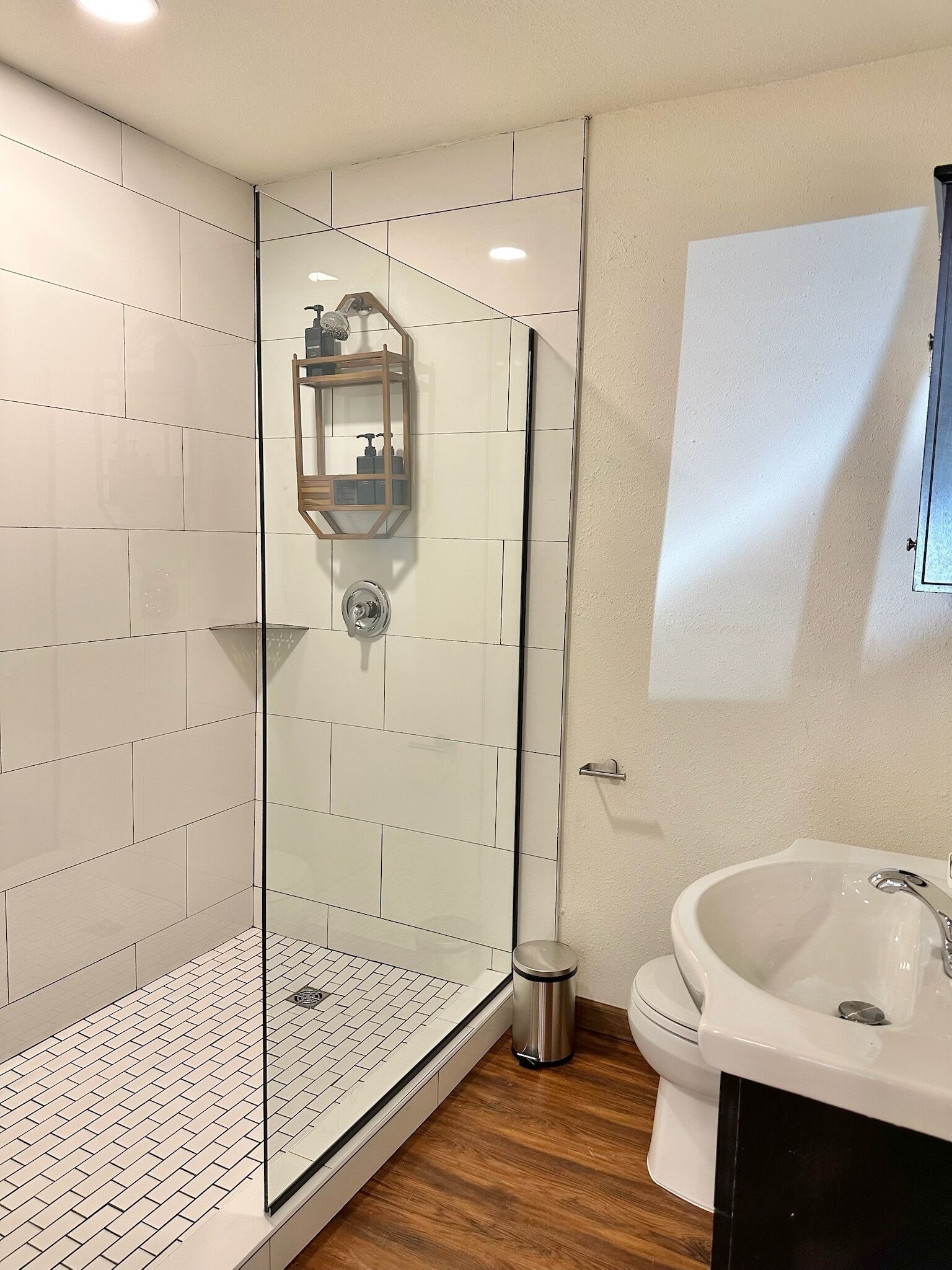 A modern bathroom with a glass-enclosed shower, a white sink, and a wooden floor.