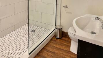 A modern bathroom with a glass-enclosed shower, a white sink, and a wooden floor.