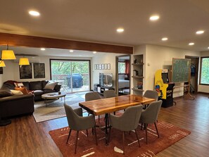 A modern living room with a wooden dining table, grey chairs, a sofa, and a TV.