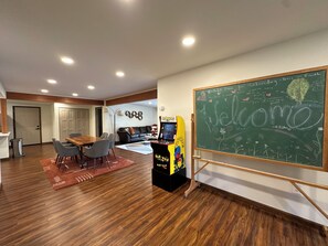 Una habitación con una pizarra, una mesa con sillas, un sofá y una máquina arcade de Pac-Man.