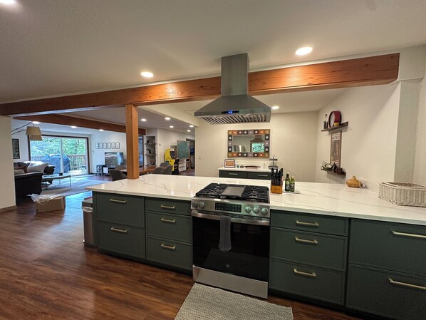 A modern kitchen with a large island, built-in appliances, and a wooden ceiling.