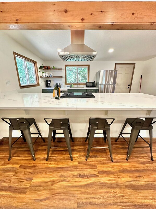 A modern kitchen with a large island, bar stools, and a stainless steel refrigerator.