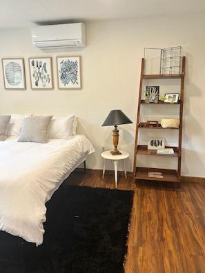Un dormitorio con una cama, una alfombra negra, suelo de madera, una lámpara y una estantería.