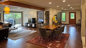 A spacious living area with a large wooden dining table, comfortable seating, a television, and a balcony with a barbecue grill. - Large Cabin on Ave of Giants with private Eel River access (Miranda)