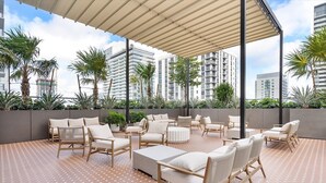 An outdoor seating area with multiple chairs and tables, surrounded by palm trees and a patterned floor.
