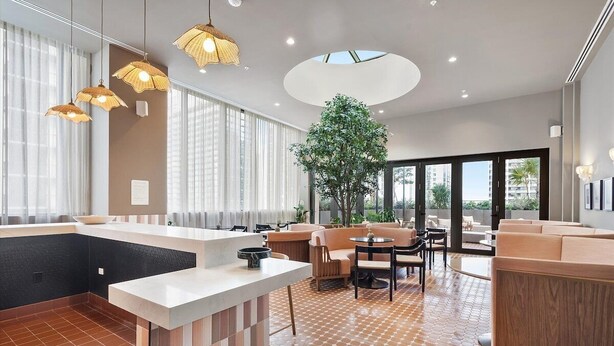 A modern hotel lobby with a central bar, seating area, and a large indoor plant.