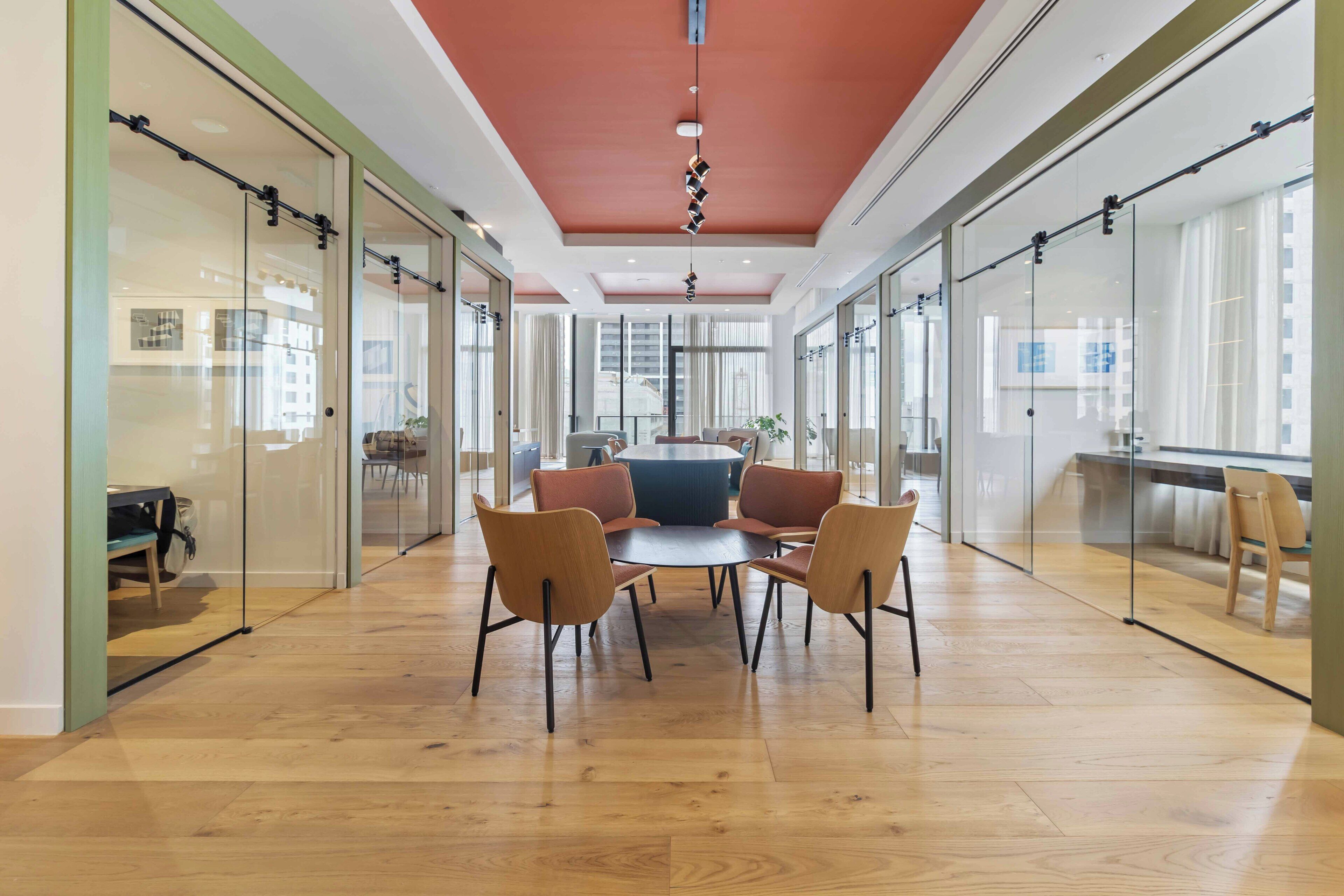 Een moderne vergaderruimte met glazen wanden, een houten vloer en een centrale tafel met stoelen.
