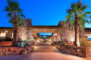 Ein Hotel mit Eingang, Steinwänden, Palmen und einer Treppe zum Foyer.