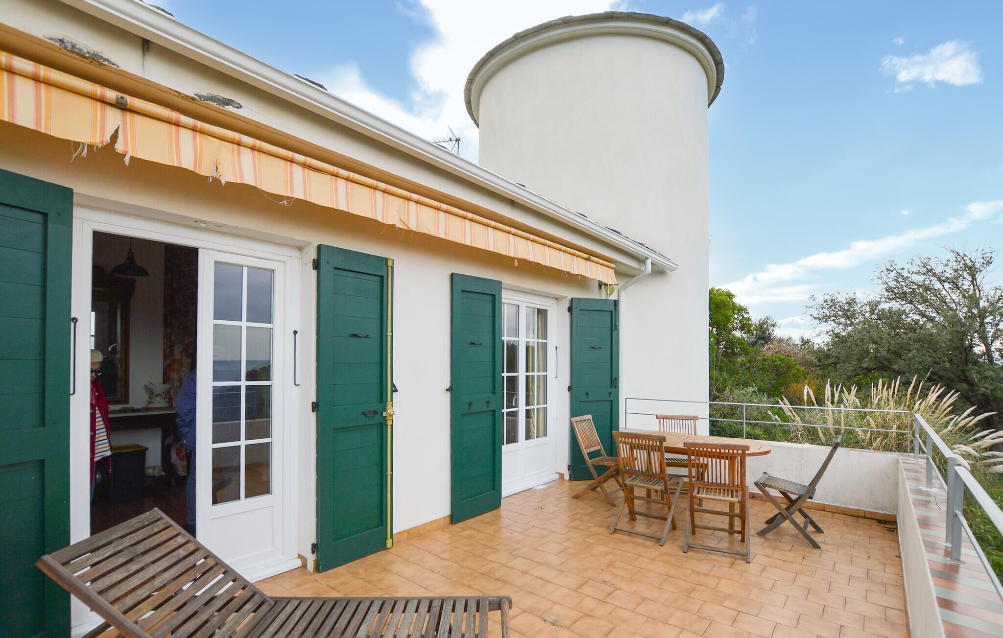 A building with a white exterior, green shutters, and a tiled patio area with wooden furniture.