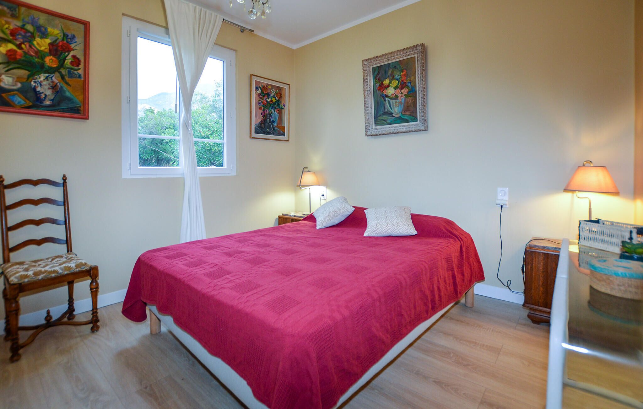 A bedroom with a large bed, two bedside lamps, a chair, and two paintings on the wall.