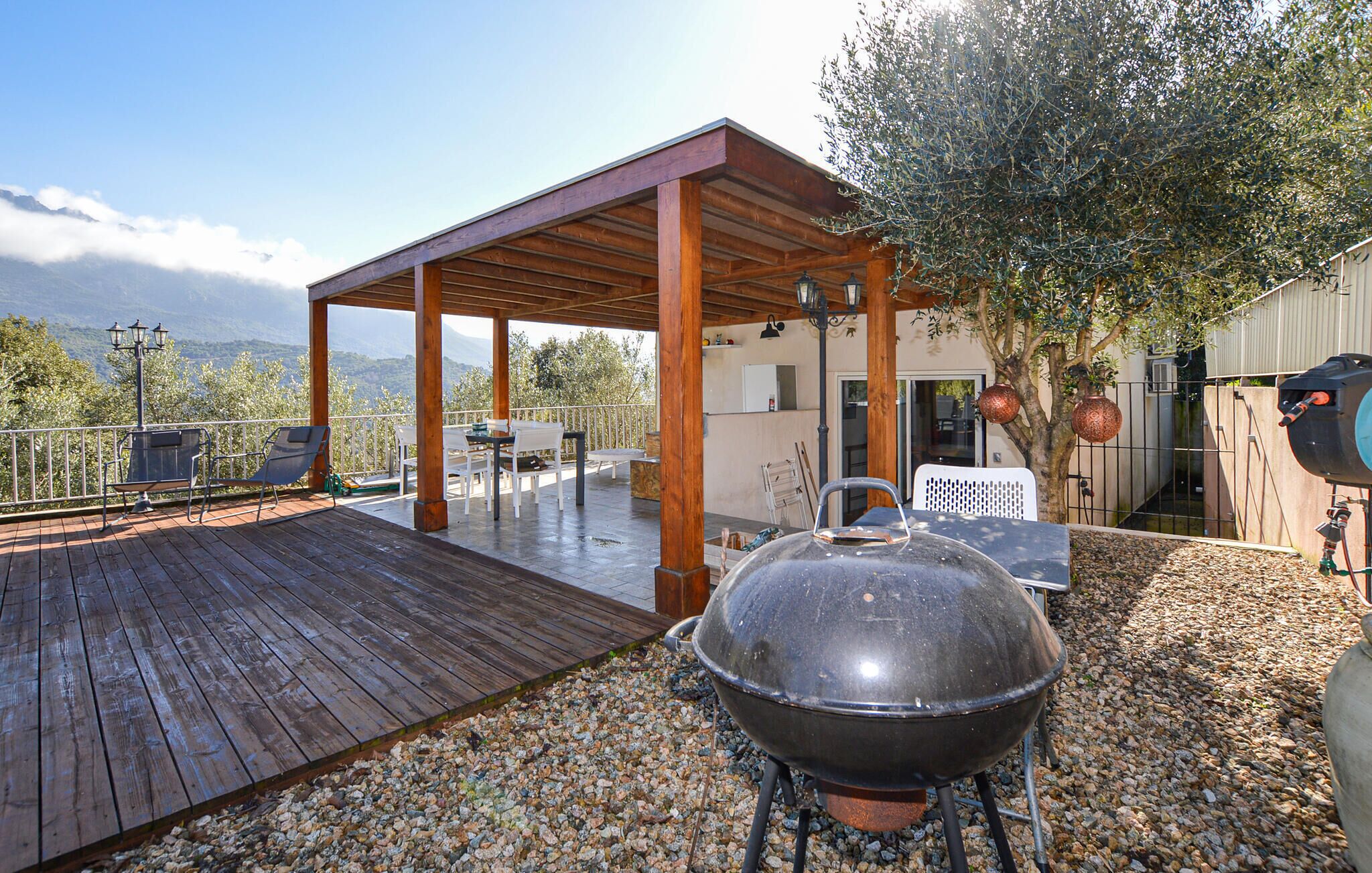 Une terrasse extérieure couverte avec une plateforme en bois, un barbecue et une vue sur les montagnes.