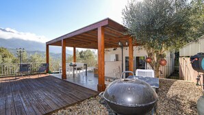 A covered outdoor patio with a wooden deck, a barbecue grill, and a view of mountains. - Stunning home in Vero with private swimming pool, can be inside or outside (Vero)