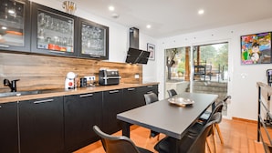 A modern kitchen with dark cabinetry, a wooden countertop, and a dining area with a large table and chairs. - Stunning home in Vero with private swimming pool, can be inside or outside (Vero)