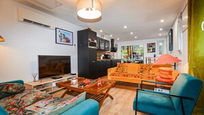 A modern living room with a sofa, a TV, and a coffee table. There is a kitchen area with cabinets and a dining table. - Stunning home in Vero with private swimming pool, can be inside or outside (Vero)