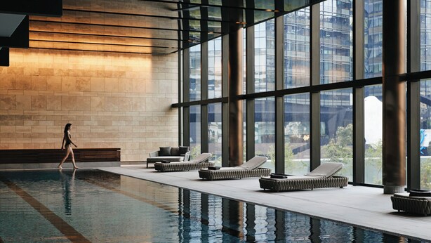 Un espace piscine intérieur moderne, avec des chaises longues et une personne qui passe.