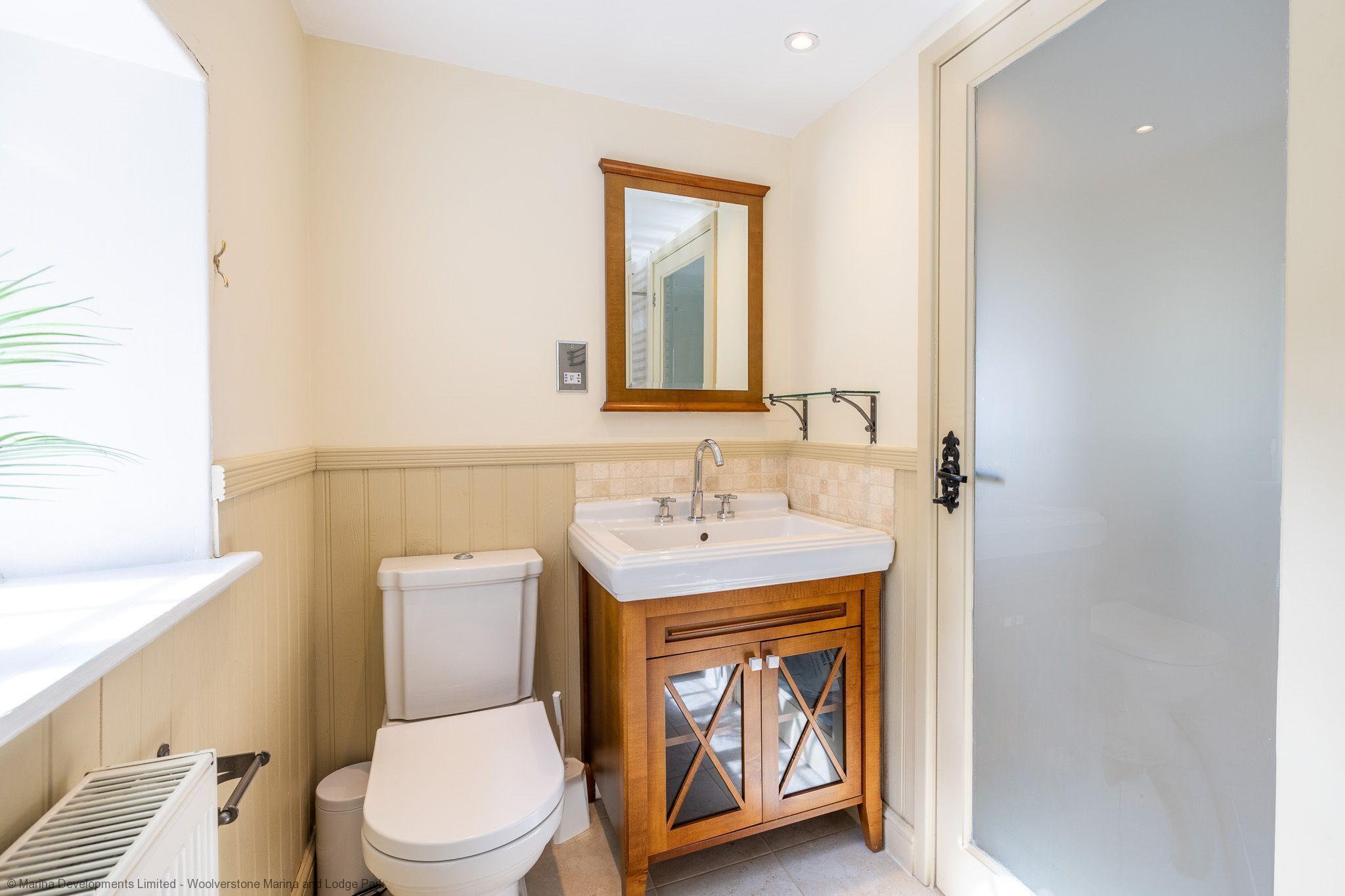 Une petite salle de bain avec des toilettes blanches, un meuble-lavabo en bois et un miroir au-dessus du lavabo.
