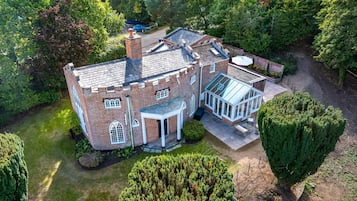 A large, two-story brick house with a conservatory, surrounded by lush greenery and a well-maintained lawn.
