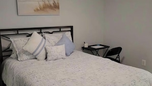 Un dormitorio con cama, una mesita, una silla y un cuadro en la pared.