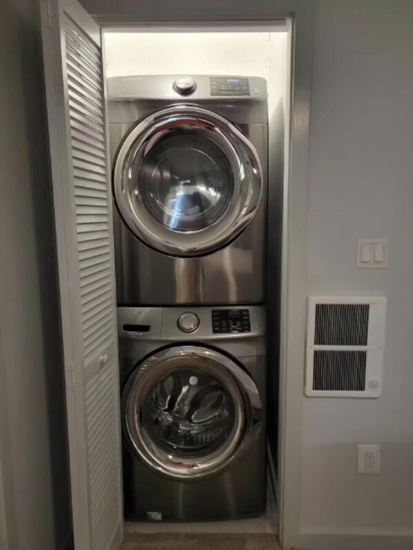 Una unidad compacta de lavadora y secadora de acero inoxidable, con panel de control, ubicada en un pasillo estrecho.