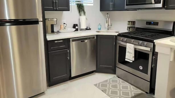 Una cocina moderna con electrodomésticos de acero inoxidable, armarios oscuros y suelo estampado.