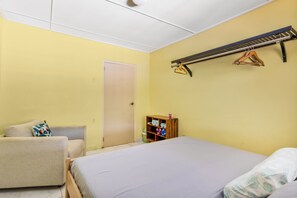 A room with a bed, a chair, a wooden shelf with items, and a door.