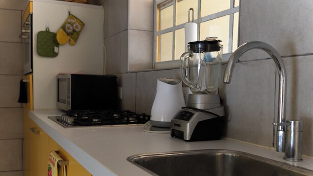 Een keuken met een roestvrijstalen spoelbak, een blender, een broodrooster en een raam met jaloezieën.