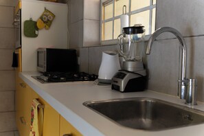 A kitchen with a stainless steel sink, a blender, a toaster, and a window with blinds.