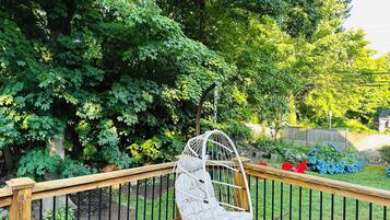 A wooden deck with a hanging chair, surrounded by lush greenery and a wooden fence.
