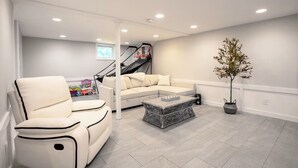 A modern living room with a sectional sofa, a coffee table, a chair, a staircase, and a potted plant. - Family Cottage with 4 King Beds  (Norwalk)