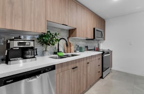 Una cocina moderna con armarios de madera, lavavajillas integrado, cafetera, microondas y fregadero.