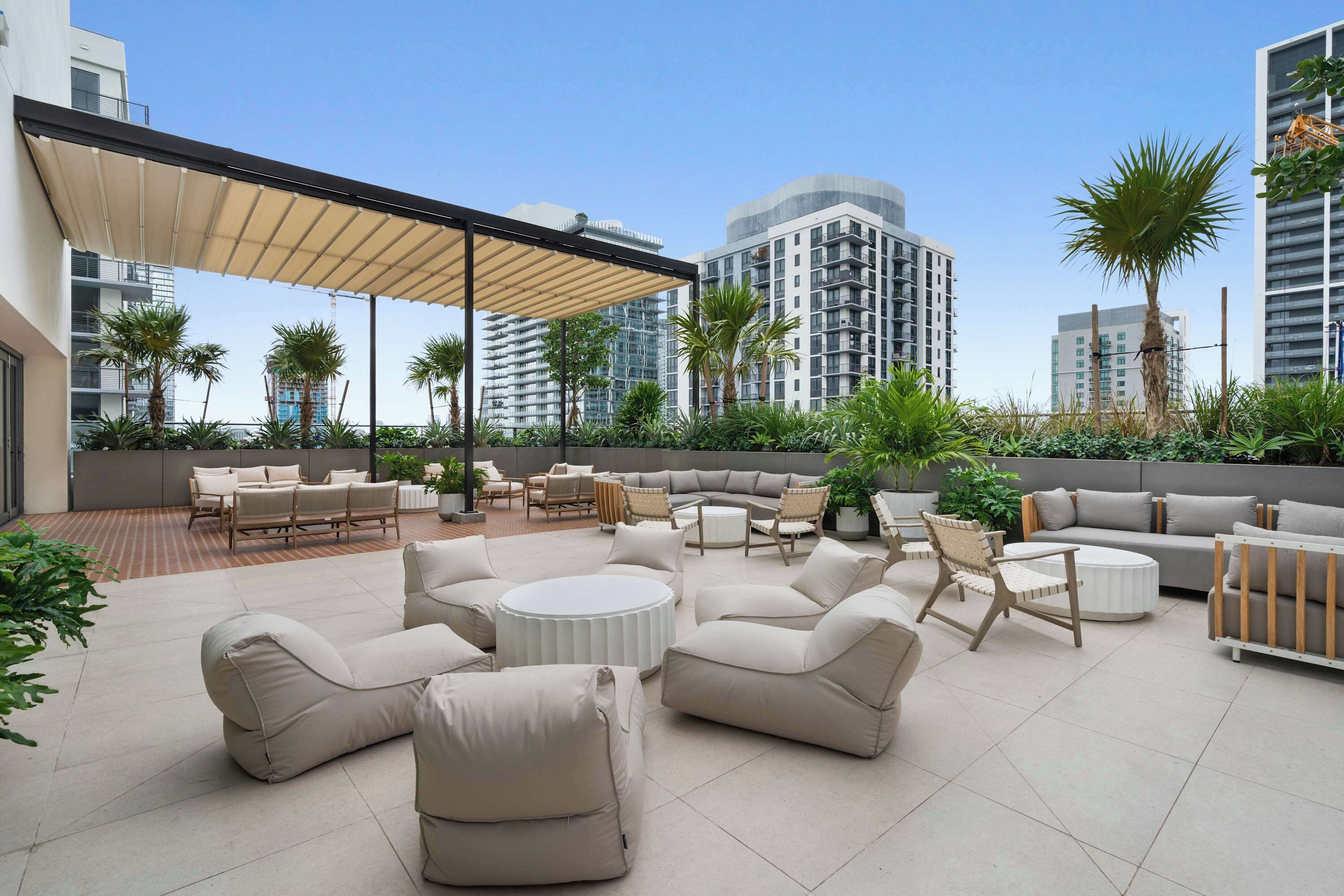 Une terrasse sur le toit, aménagée avec du mobilier d’extérieur, des palmiers et des bâtiments modernes en arrière-plan.