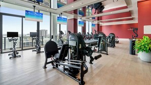Ein Fitnessstudio mit verschiedenen Trainingsgeräten, großen Fenstern und Blick auf die Stadt.