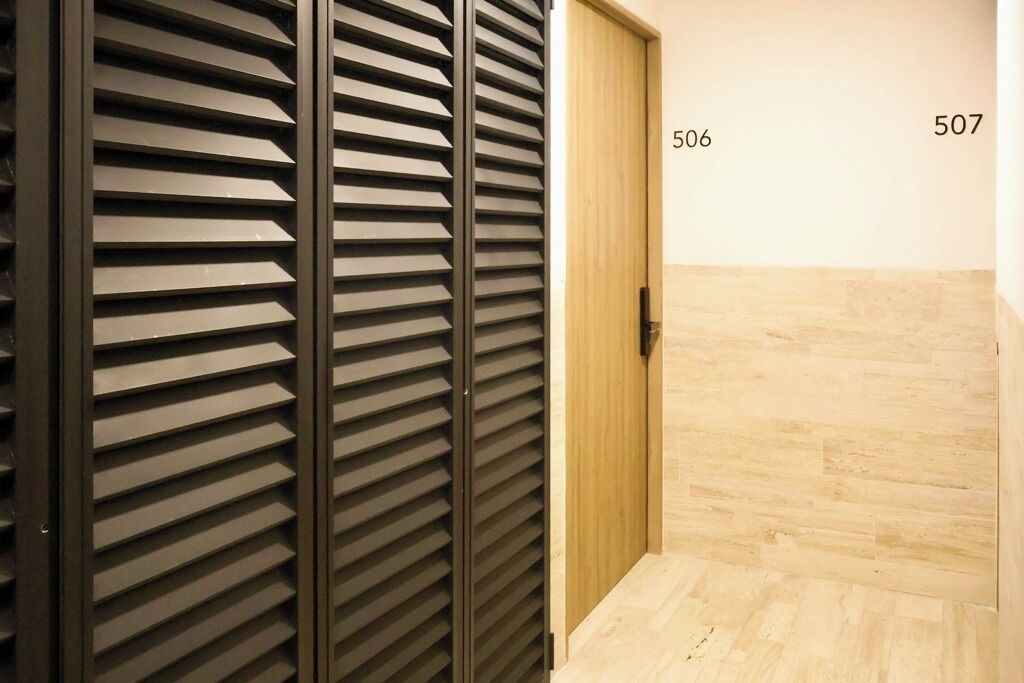 Ein Korridor mit einer Holztür, auf der die Nummer 506 steht, und einem schwarzen Metallabtrenner.