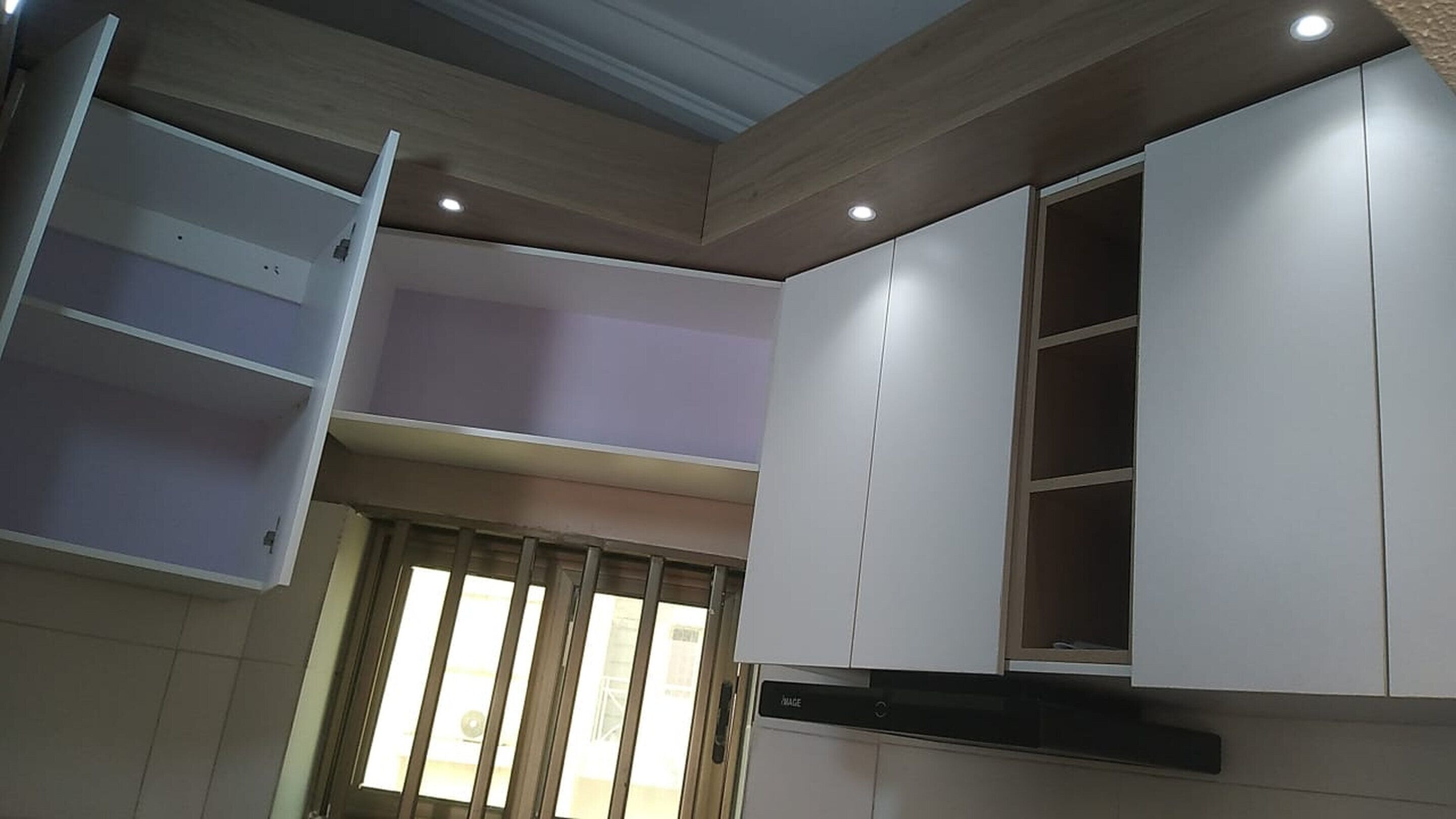 A kitchen with white cabinets, a built-in oven, and a window with blinds.