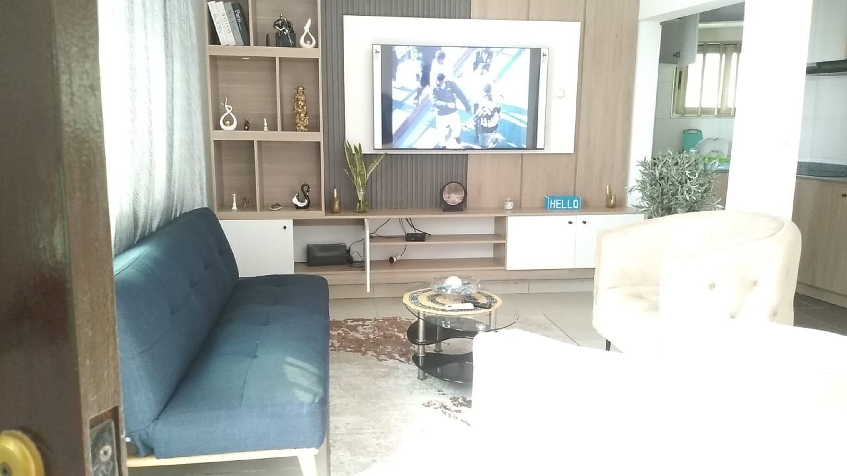 A living room with a blue sofa, a white armchair, a coffee table, and a TV mounted on the wall.