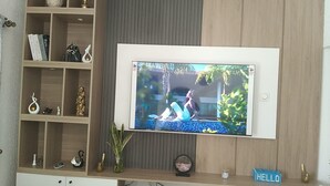 Un televisor de pantalla plana sujeto a una pared de madera, con un estante inferior que exhibe diversos objetos decorativos.