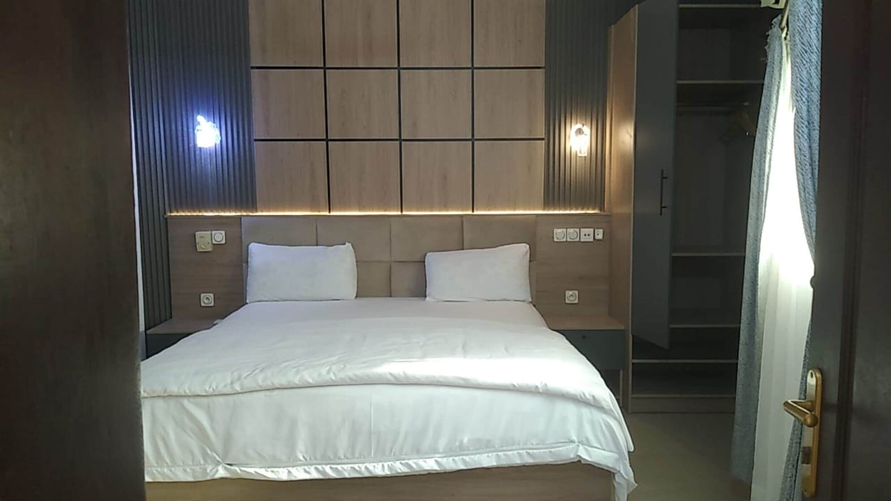 A neatly made bed with a headboard, bedside tables, and wall-mounted lighting.
