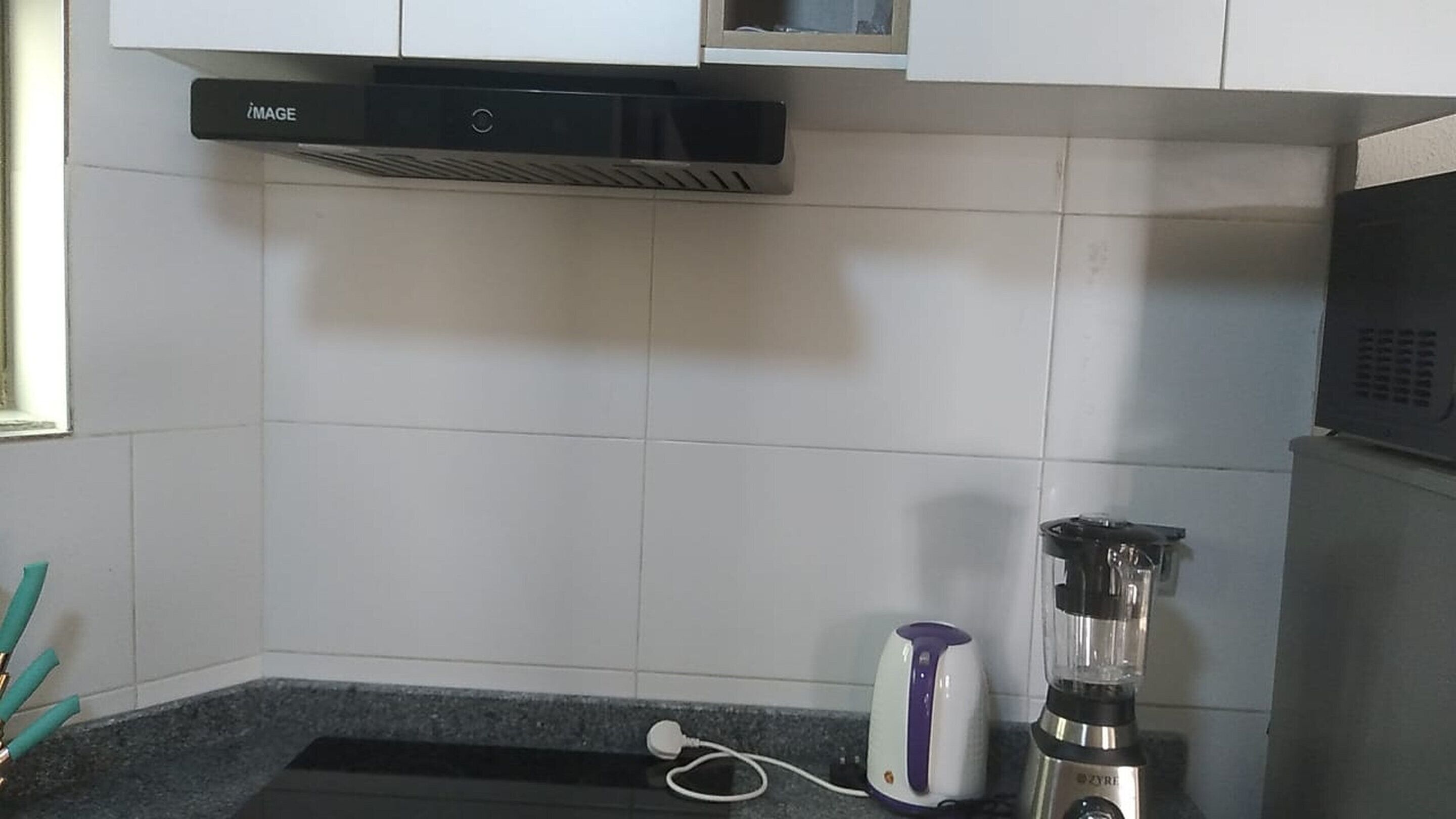 Une cuisine avec des carreaux blancs, un four à micro-ondes encastré, une bouilloire et un mixeur posés sur le plan de travail.