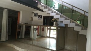 Una escalera con barandillas de vidrio, una pared blanca con un reloj y un florero con flores.