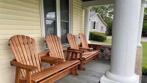 Een veranda met houten Adirondack-stoelen en een stenen pilaar.