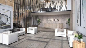 Un vestíbulo moderno con sofás blancos, un mostrador de recepción identificado como 'AQUA' y arte abstracto en las paredes.