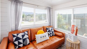 A modern living room with a brown leather sofa, geometric patterned pillows, and a small side table with a magazine holder. - Zion Tiny Home • Hot Tub •  Gooseberry Mesa Trails (Apple Valley)