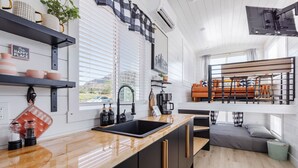 A modern kitchen with a wooden countertop, black cabinets, and a built-in oven. There is a window with blinds, a sink, and a coffee machine. - Zion Tiny Home • Hot Tub •  Gooseberry Mesa Trails (Apple Valley)