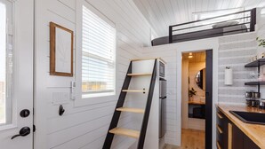 A compact kitchen with white wooden walls, a black ladder shelf, and a small dining area with a window. - Zion Tiny Home • Hot Tub •  Gooseberry Mesa Trails (Apple Valley)