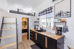 Uma cozinha compacta com armários pretos, bancada de madeira e uma máquina de café preta.
