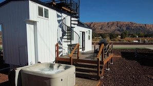 A spa building with a hot tub, wooden deck, and a staircase leading to a balcony. - Private Hot Tub + Rooftop Deck • Near Zion National Park (Apple Valley)