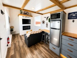 A compact kitchen with a refrigerator, a microwave, and a stove. There is a small seating area with a couch and a table. - Zion Couples’ Retreat • Romantic Desert Tiny Home (Apple Valley)