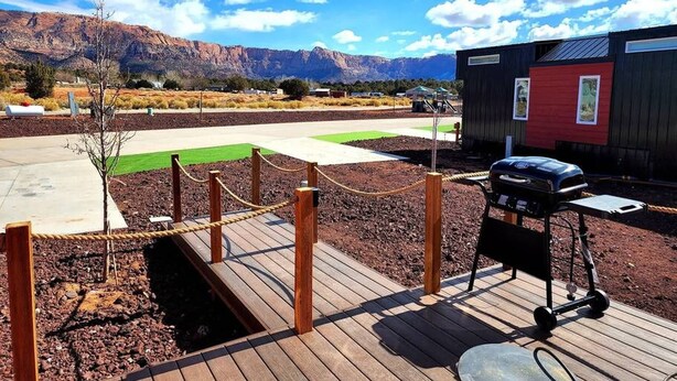 A wooden deck with a barbecue grill, a small red building, and a mountain view in the background. - Zion Couples’ Retreat • Romantic Desert Tiny Home (Apple Valley)